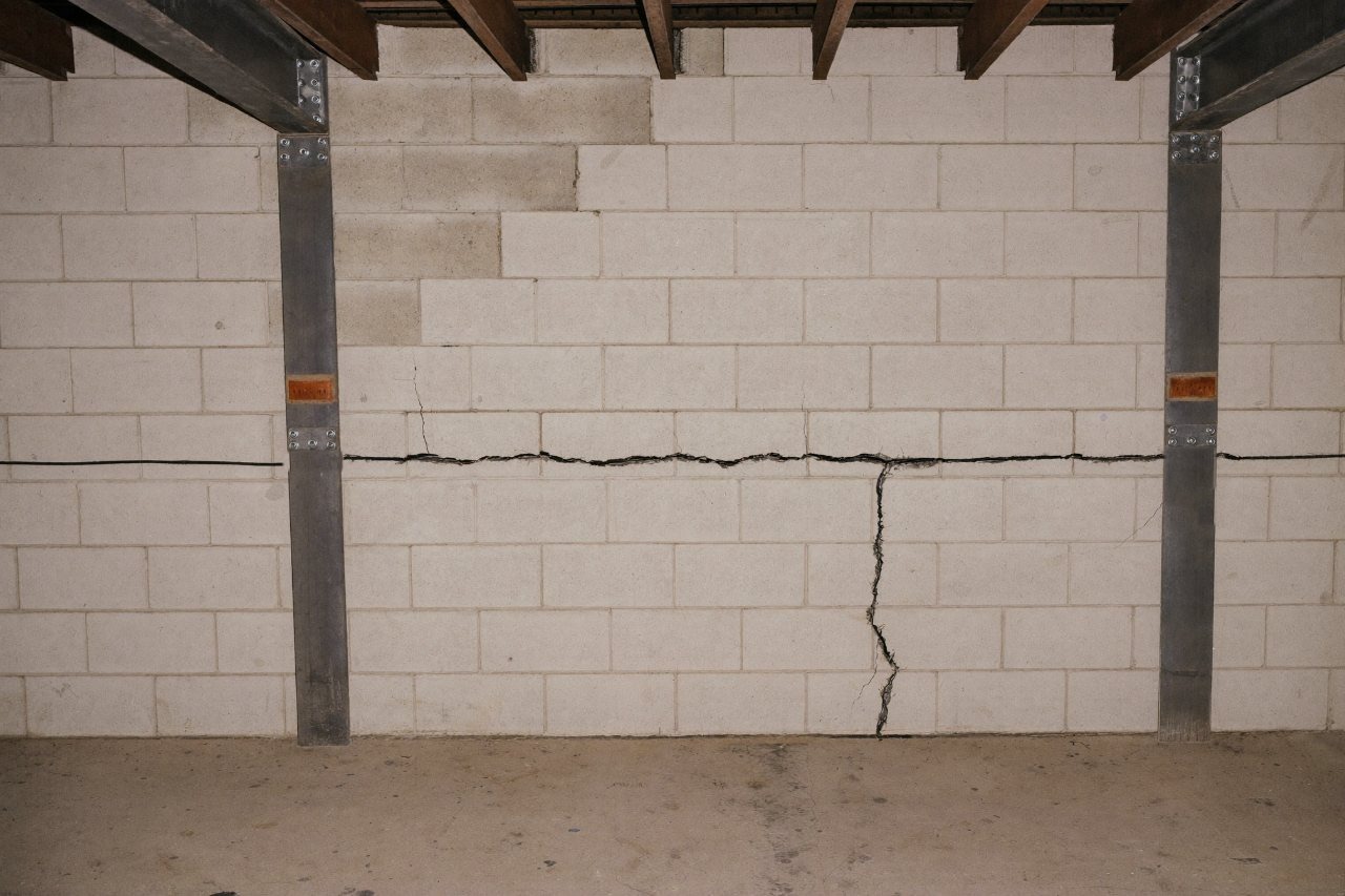 A concrete block basement wall bowing inward with a long horizontal crack along a mortar joint and steel reinforcement beams anchored against it