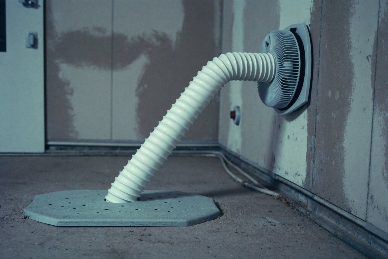 A radon mitigation system with a white PVC suction pipe rising from the slab to an inline fan along a basement wall