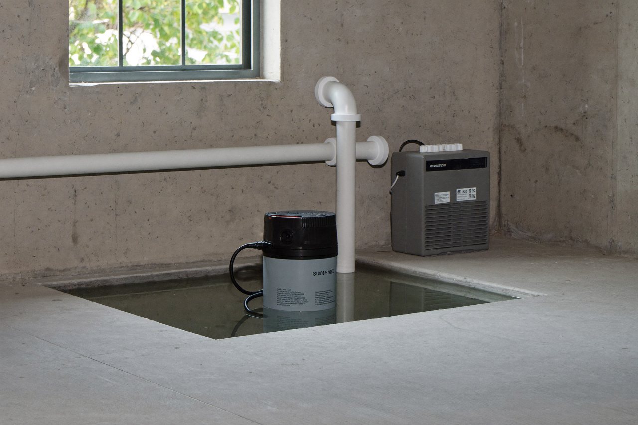 A sump pump in an open sump basin with a discharge line and battery backup unit in a clean basement