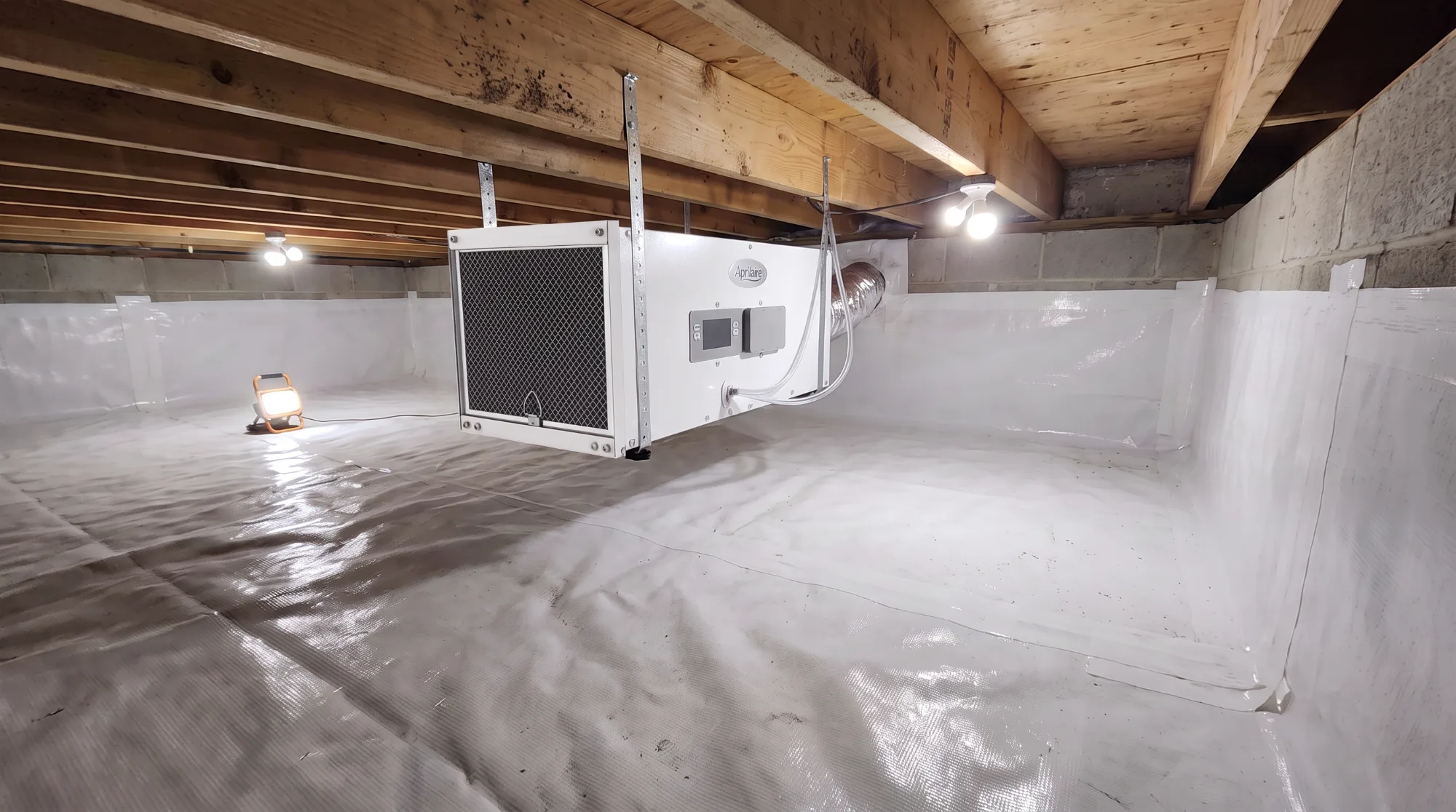 Encapsulated crawl space with white vapor barrier sealed across the floor and walls and a ceiling-mounted dehumidifier