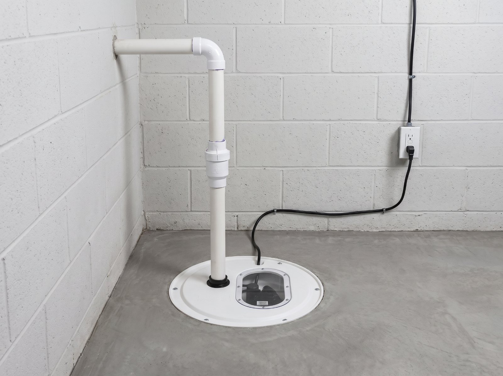 Newly installed sump basin with a sealed lid, check valve and PVC discharge line in a basement floor