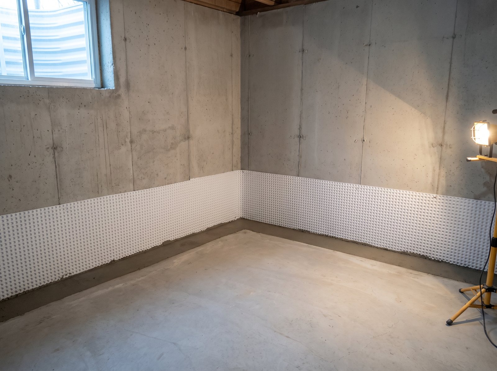 Basement corner after interior waterproofing, with a sealed perimeter channel and drainage membrane on the wall